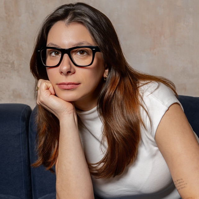 Victoria Giroto de óculos e camiseta branca, sentada em um sofá azul